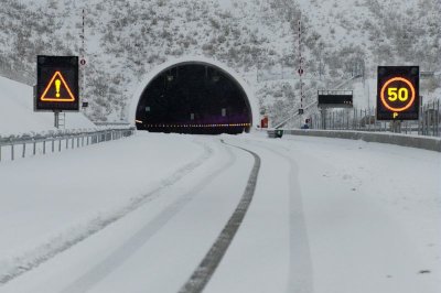 Une route enneigée menant à un tunnel, des panneaux limite la vitesse à 50km/h 